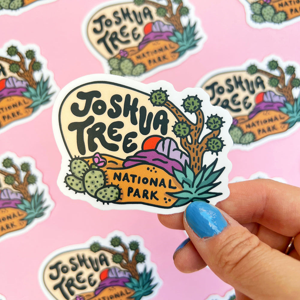 Sticker with 'Joshua Tree National Park' design held by a hand on a pink background