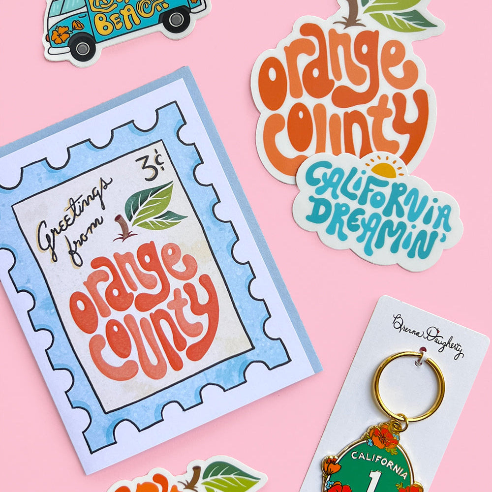 Orange County-themed products including a card, keychain, and stickers on a pink background
