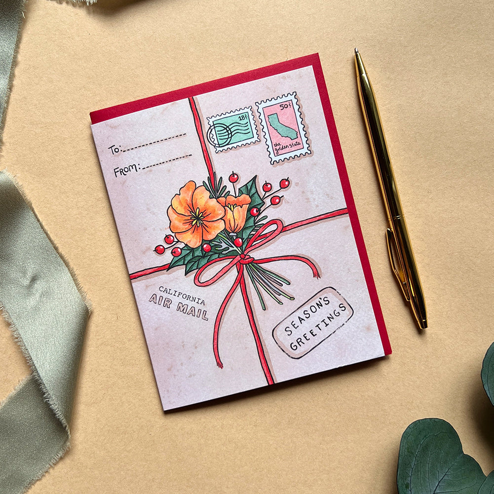 Greeting card with floral design and stamps on a beige surface with a pen and ribbon.