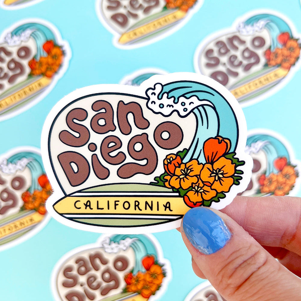 Sticker with 'San Diego, California' design held by a hand on a blue background
