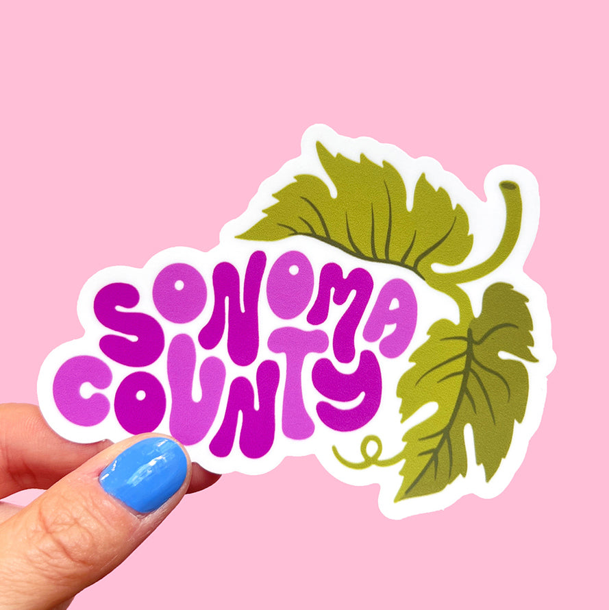 Sonoma County wine country grape sticker being held to show scale on pink background