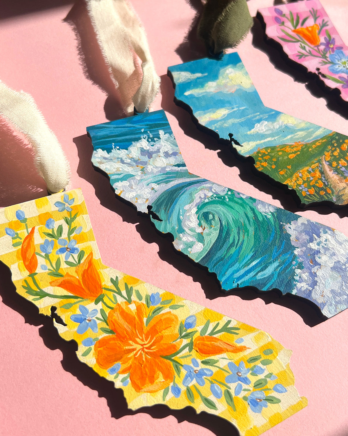 Colorful painted California ornaments with nature-themed designs on a pink background