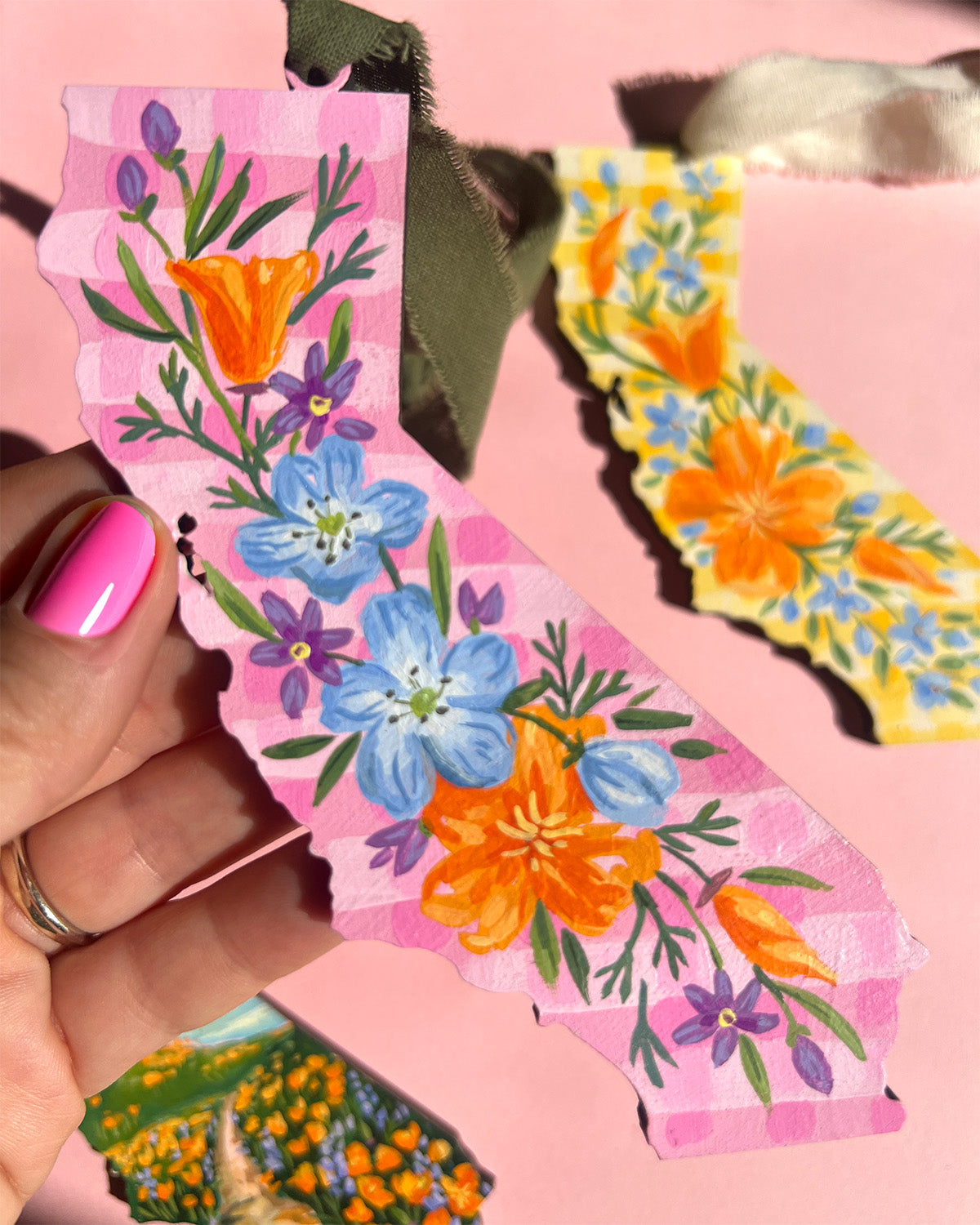 California shaped painting held by a hand with pink nail polish