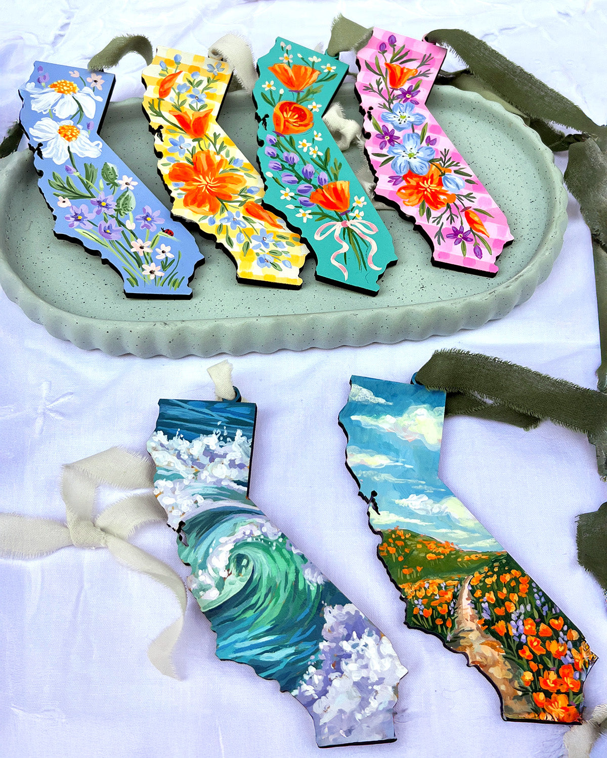Decorative ornaments shaped like California with floral and ocean designs on a white surface.