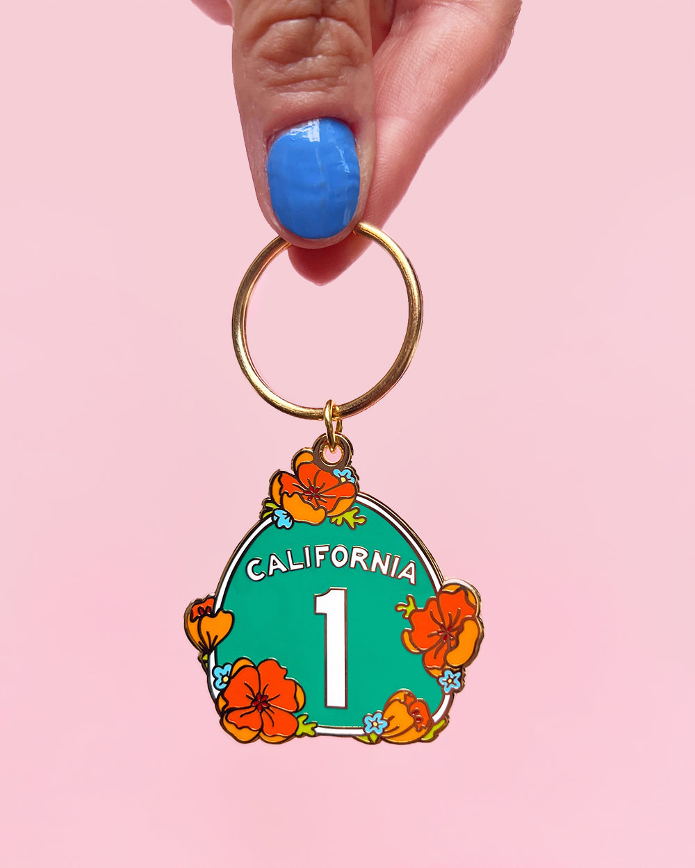 Highway 1 California poppy hard enamel keychain being held to show scale