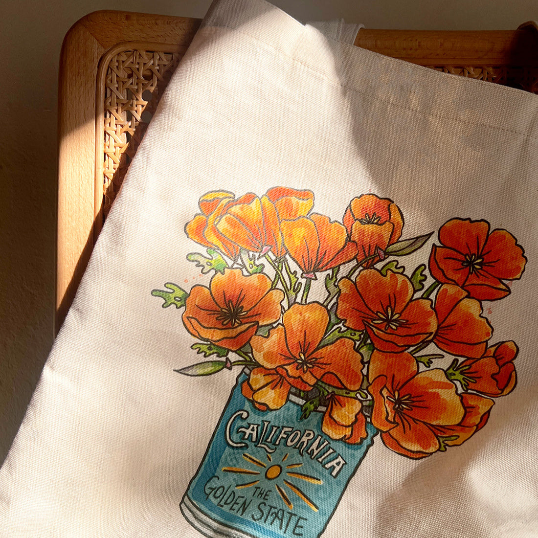 Tote bag with poppies and 'California The Golden State' design on a wooden surface.